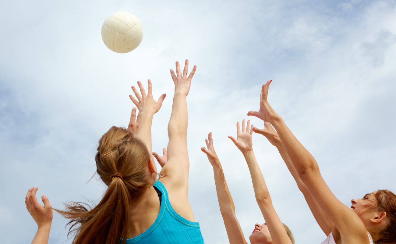 A photograph looking up to the sky. A group of people are reaching up to catch a ball.
