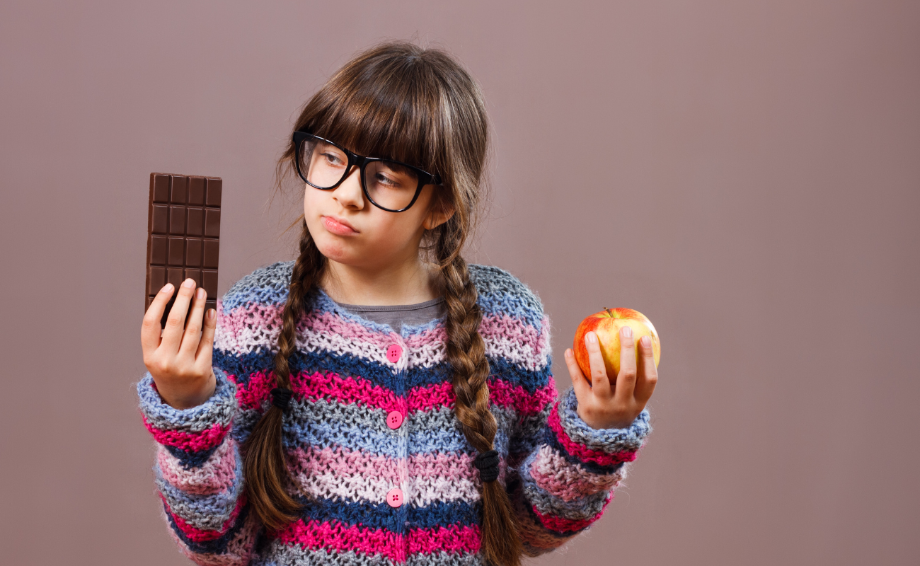 A photograph of a child holding a bar of chocolate in one hand and an apple in the other.